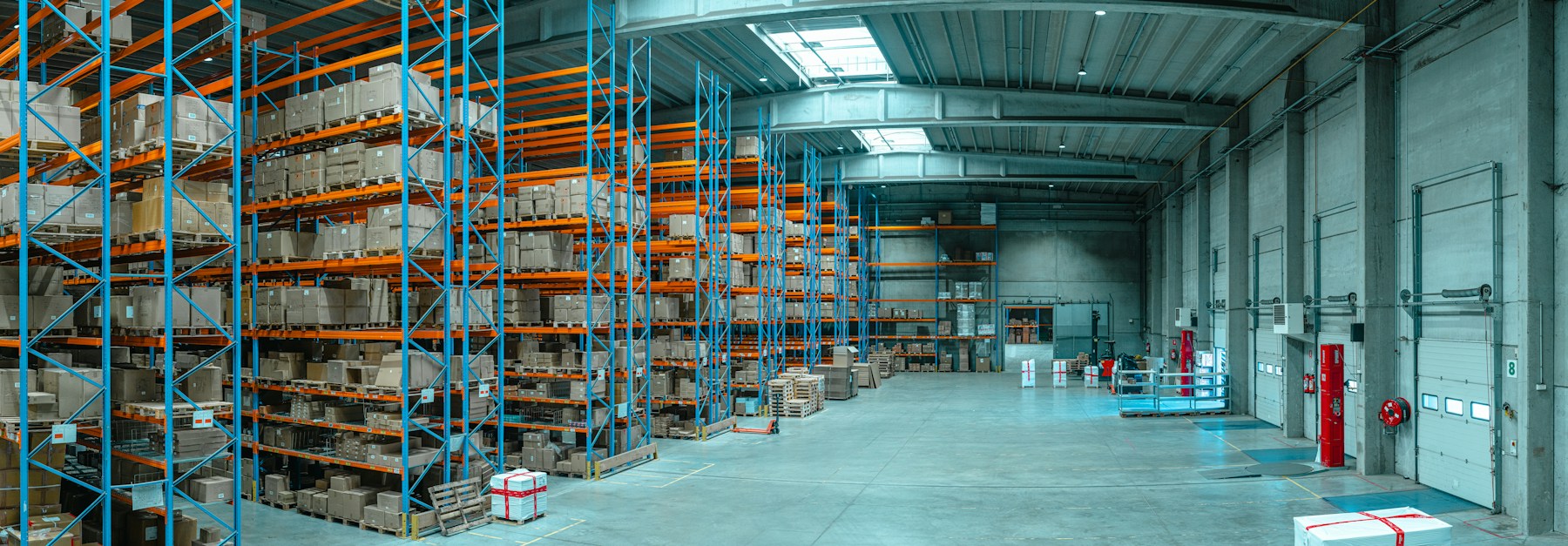 Cardboard boxes on tall blue and orange racks beside loading bays in a warehouse